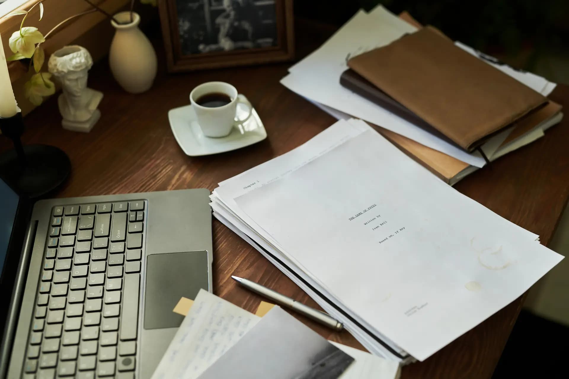 A printed book manuscript, laptop, pen, and cup of coffee on a wooden writer’s desk